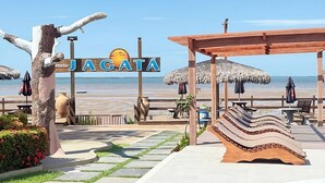 Un resort frente a la playa con un letrero que dice 'JAGATA', asientos al aire libre, una piscina y vista al océano.
