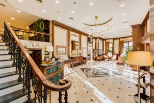 Un lobby espacioso con una escalera de mármol, un candelabro y una recepción.