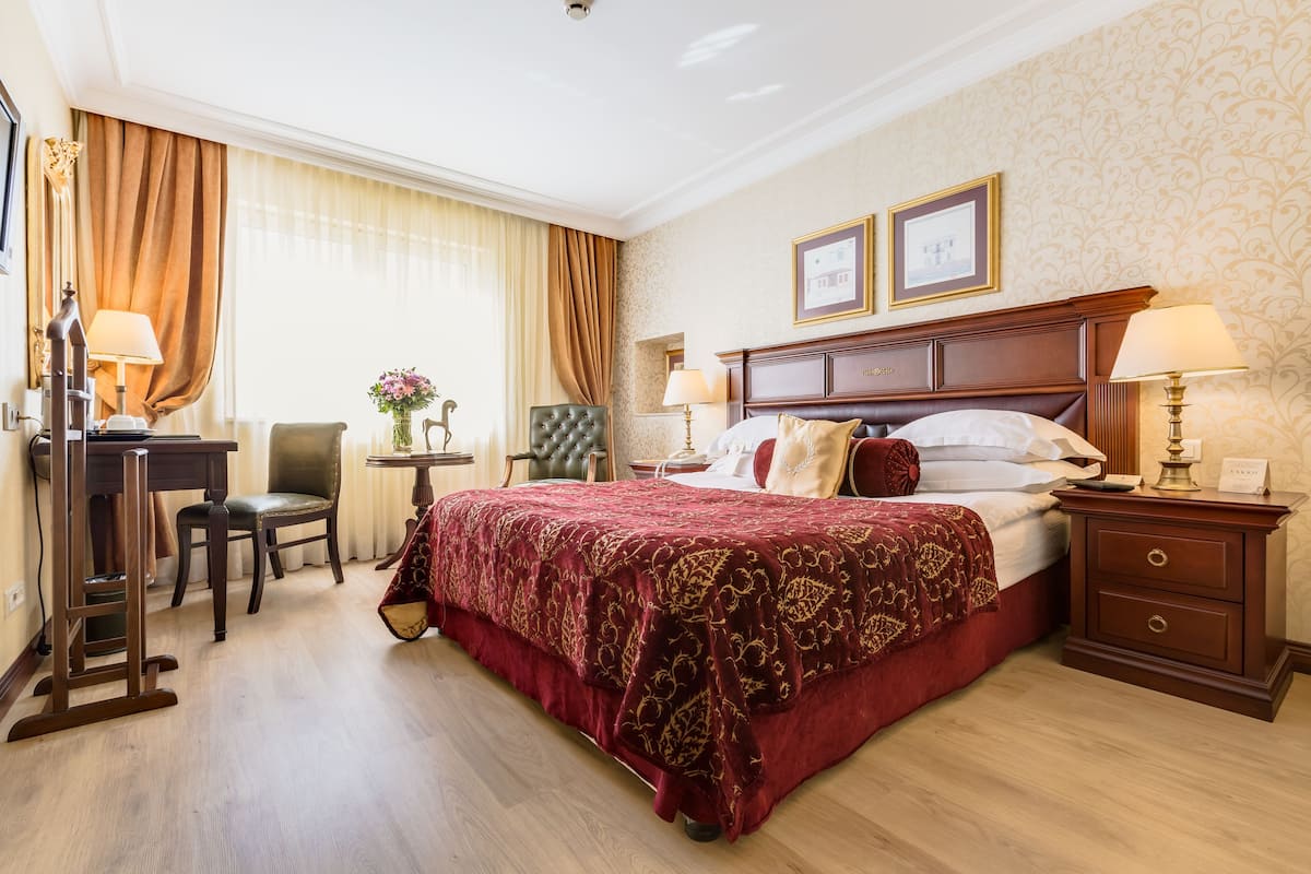 Habitación de hotel con una cama grande, un escritorio, una silla y una mesita con un florero.