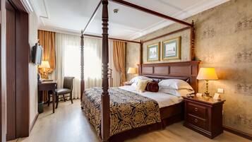 A four-poster bed with a patterned bedspread, a bedside table with lamps, and a desk with a chair.
