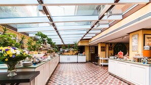 A spacious, well-lit atrium with a high ceiling and skylights, featuring a central island with a variety of food items and a decorative vase of flowers. - Gordion Hotel - Special Class (Ankara)