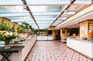 Un amplio y luminoso atrio con techo alto y tragaluces, que presenta una isla central con diversas opciones de comida y un florero decorativo.