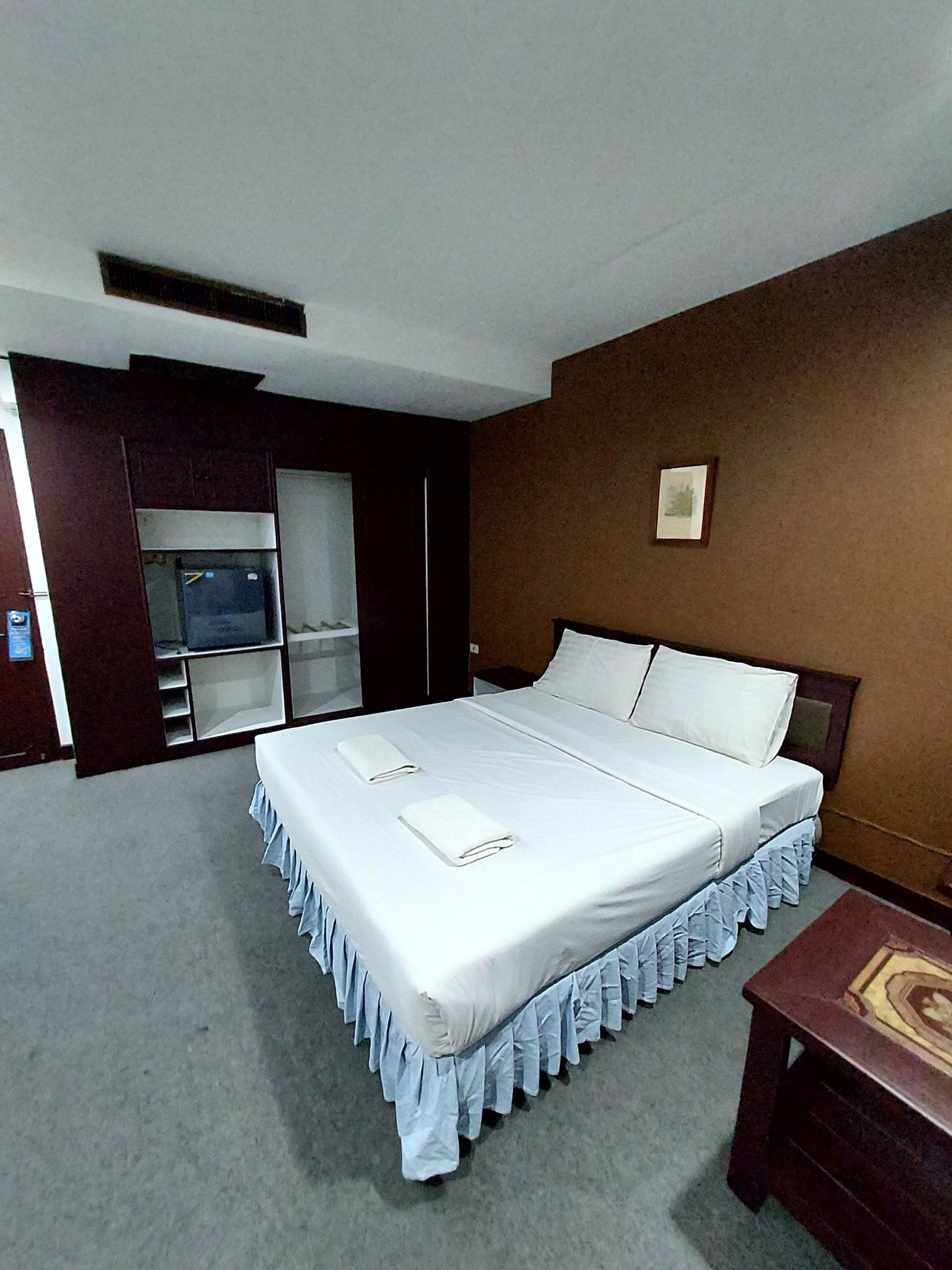 A hotel room with a large bed, a wardrobe, a small table, and a picture on the wall.