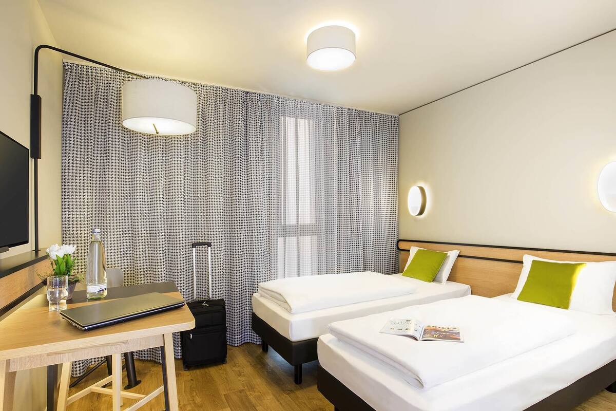 Een hotelkamer met een bureau, twee bedden, een televisie en een raam met gordijnen.