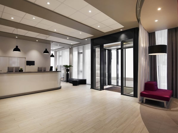 A modern reception area with a counter, seating, and a large glass door leading outside. - Aparthotel Adagio Access Muenchen City Olympiapark (Munich)