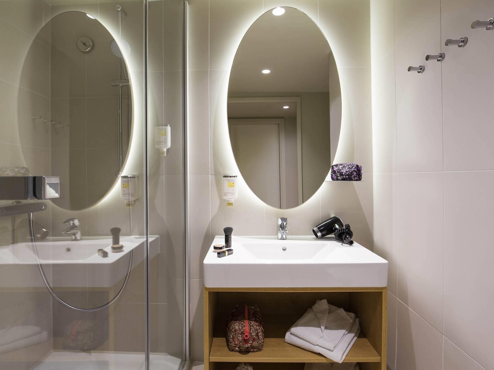 A modern bathroom with a glass-enclosed shower, a vanity with a mirror, and a shelf with towels and toiletries.