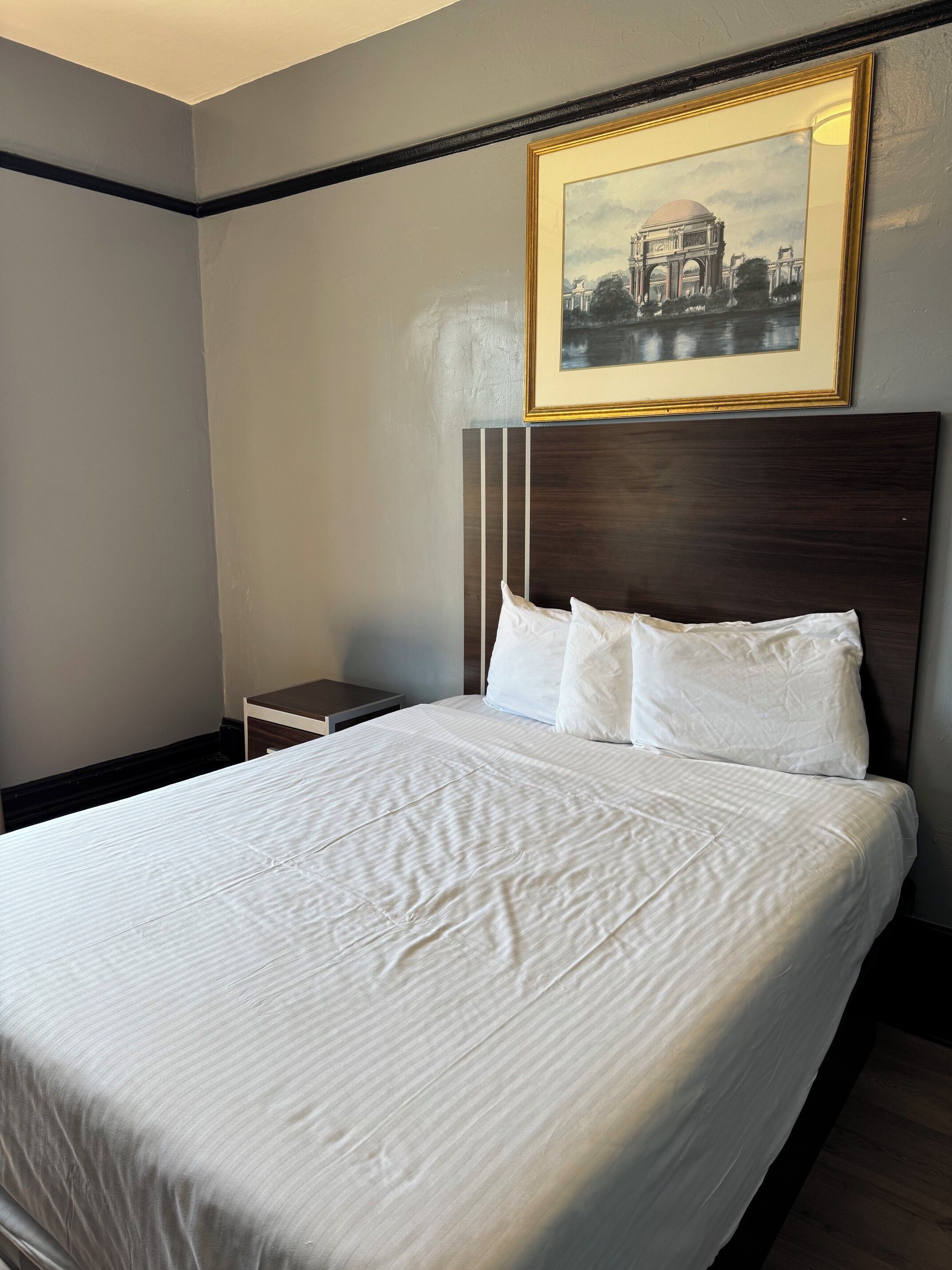 Habitación de hotel con una cama grande, una mesita de noche, un cuadro enmarcado en la pared y un cabecero de madera oscura.