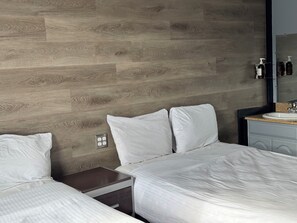 A hotel room with a wooden wall, a bed with white bedding, a nightstand, a mirror, and a sink. - Europa Hotel (San Francisco)