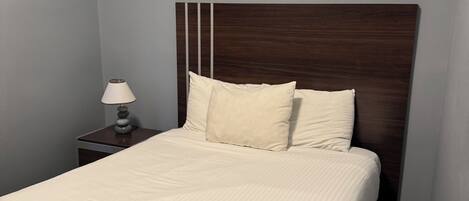 Ein ordentlich bezogenes Bett mit einem hölzernen Kopfteil, einer Nachttischlampe und einem kleinen Tisch.