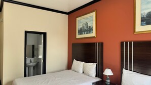 A hotel room with two beds, a nightstand with a lamp, a framed picture on the wall, and a bathroom visible through an open door. - Europa Hotel (San Francisco)