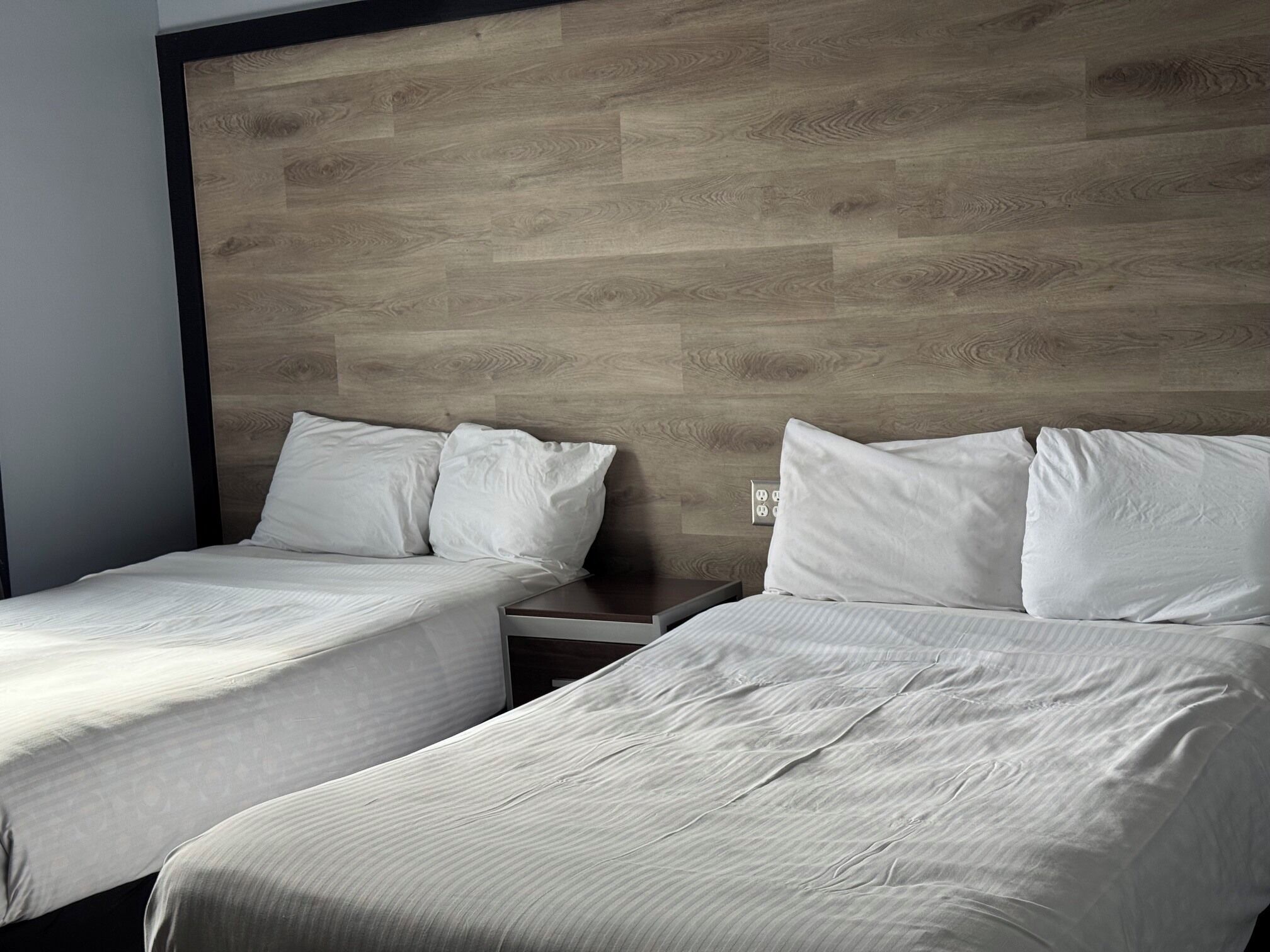 Une chambre d’hôtel avec deux lits simples, une tête de lit en bois et une table de chevet.