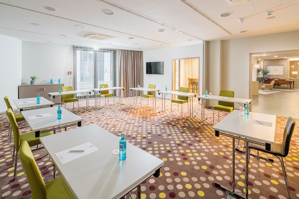 Een hotelconferentiezaal met meerdere tafels, stoelen en een vloerbedekking.