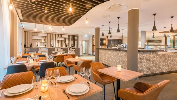 Ein Restaurant mit Holztischen, Ledersesseln und Pendelleuchten.