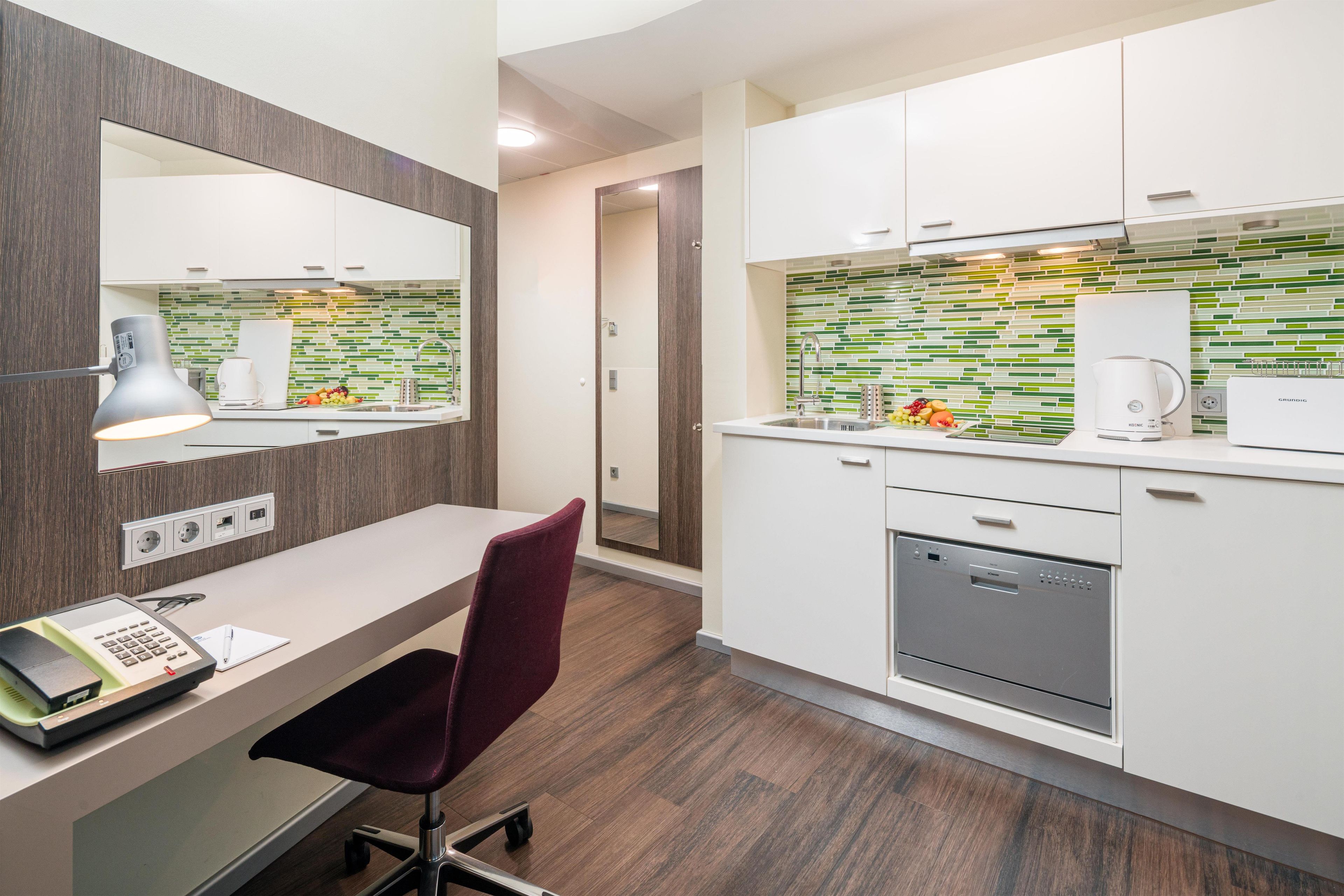 A modern kitchen with white cabinets, a built-in dishwasher, and a green-tiled backsplash.