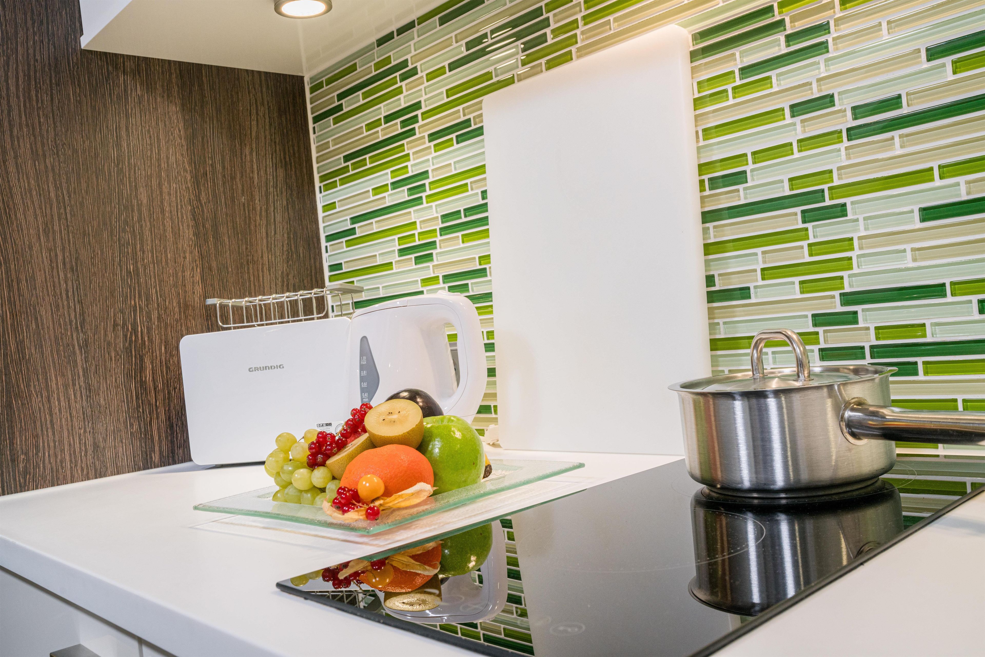 Eine Küche mit modernem Design, ausgestattet mit einer weißen Arbeitsplatte, einem Edelstahl-Wasserkocher und einem Topf auf einem Induktionskochfeld.