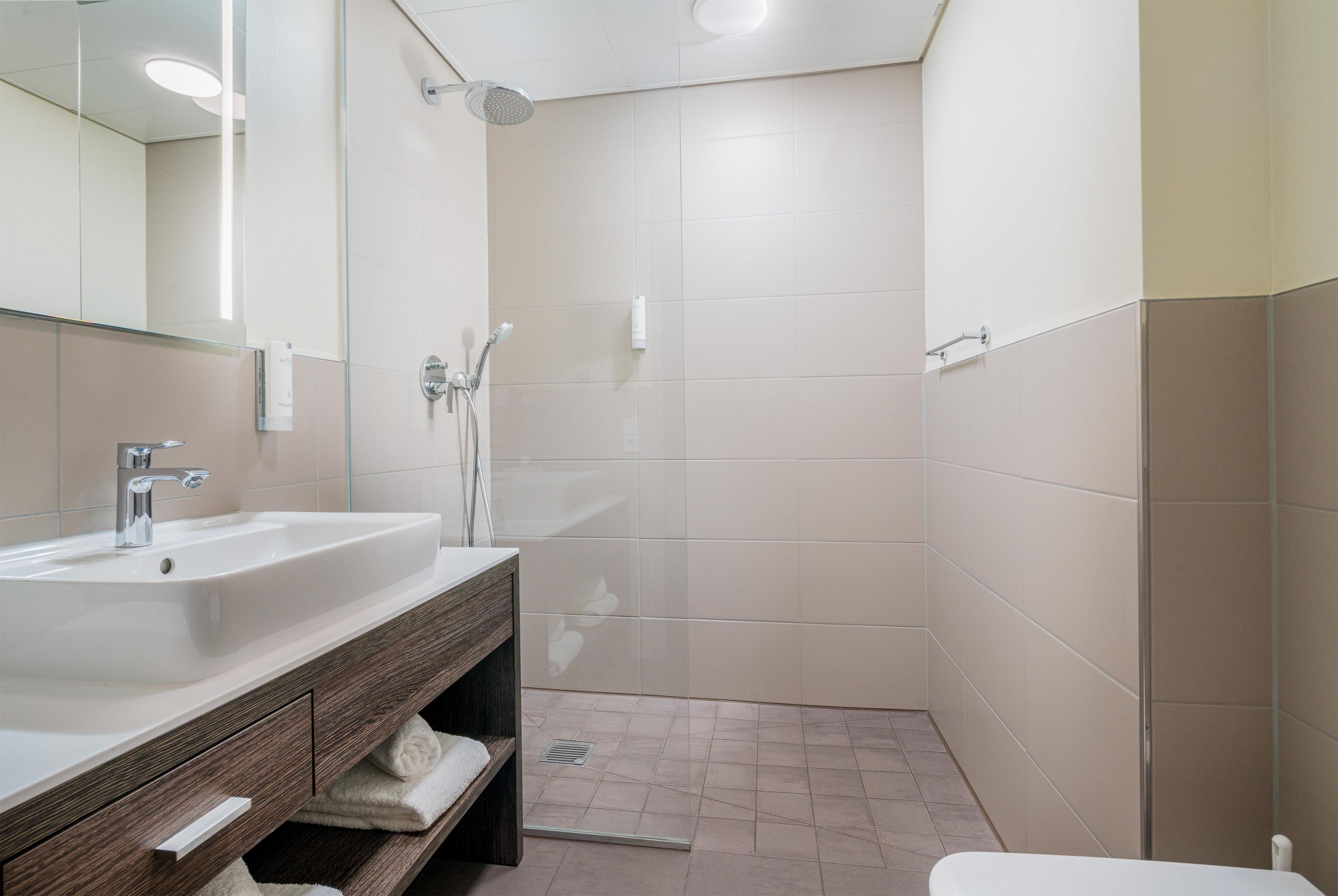 Un baño moderno con lavamanos, espejo y ducha.
