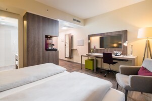 A hotel room with two beds, a desk, a chair, a TV, and a lamp.