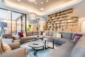 Un salon moderne avec un canapé d’angle, deux petites tables rondes et une bibliothèque intégrée.