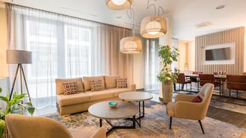 A modern living room with a sofa, coffee table, armchairs, and a dining area with a TV.
