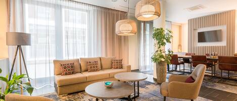 A modern living room with a sofa, coffee table, armchairs, and a dining area with a TV.