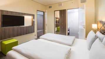 Une chambre d’hôtel avec un grand lit, une télévision, un pouf vert et une salle de bain visible à travers une porte ouverte.
