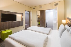 Habitación de hotel con una cama grande, televisión, un reposapiés verde y un baño visible a través de una puerta abierta.