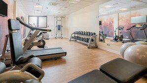 Ein Fitnessstudio mit Trainingsgeräten, darunter Laufbänder, Kurzhanteln und Kraftgeräte.