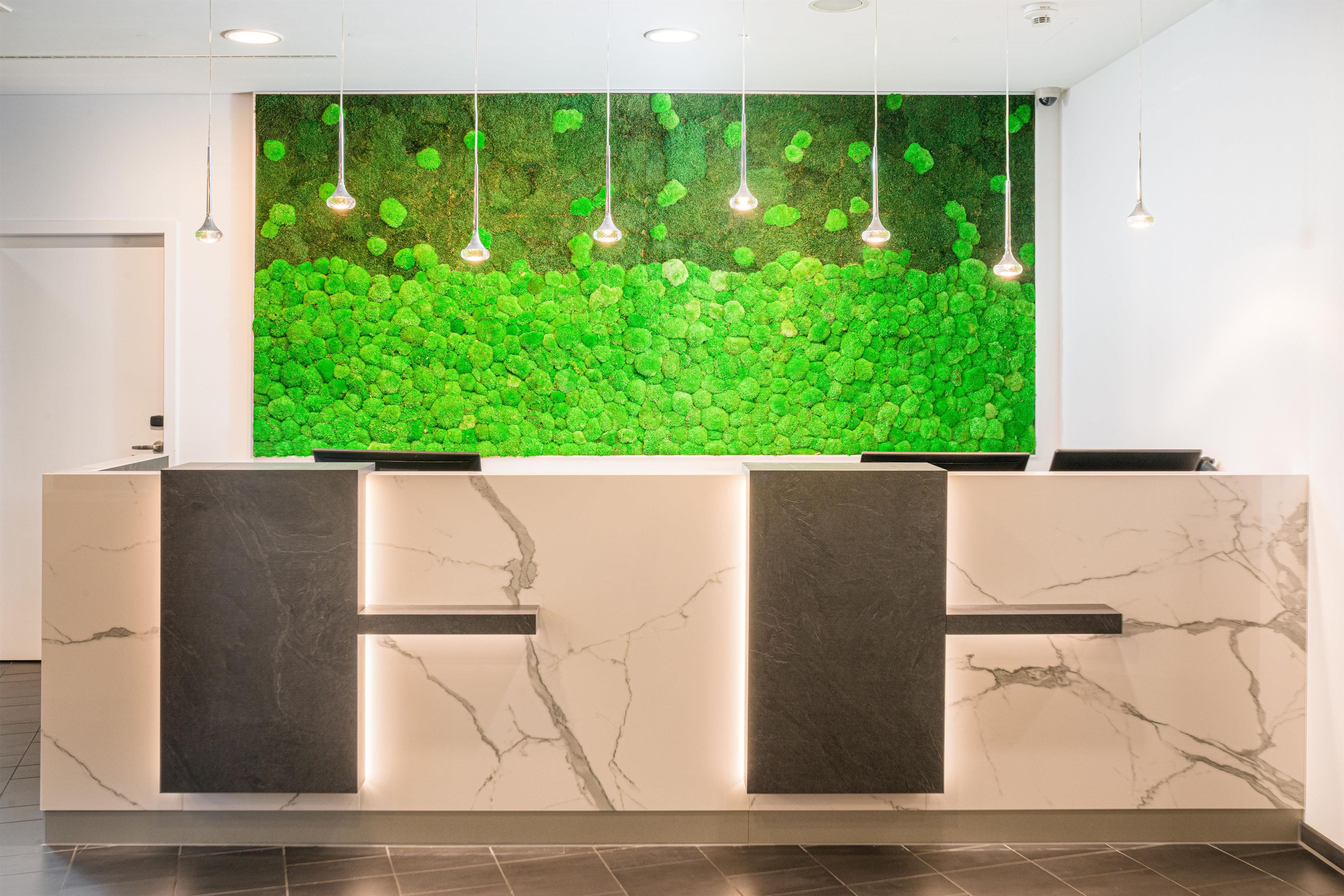 A reception desk with a green moss wall and pendant lighting.