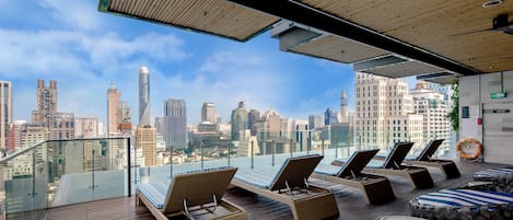 A rooftop lounge with sun loungers and a city view.