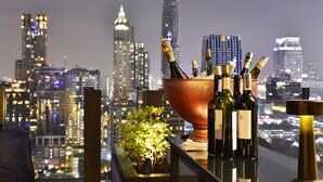 Vista panorámica de la ciudad desde un balcón, con un recipiente de cobre grande que contiene botellas de vino y una botella de champán.