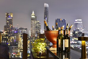 Vista panorámica de la ciudad desde un balcón, con un recipiente de cobre grande que contiene botellas de vino y una botella de champán.