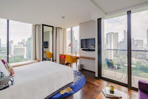 Ein modernes Hotelzimmer mit einem großen Bett, einem Schreibtisch, einem Stuhl, einem Fernseher und einem Balkon mit Blick auf die Stadt.