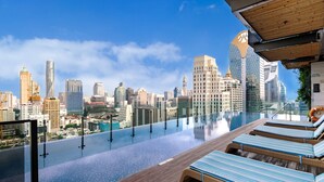 A rooftop infinity pool with lounge chairs, overlooking a city skyline with modern buildings.