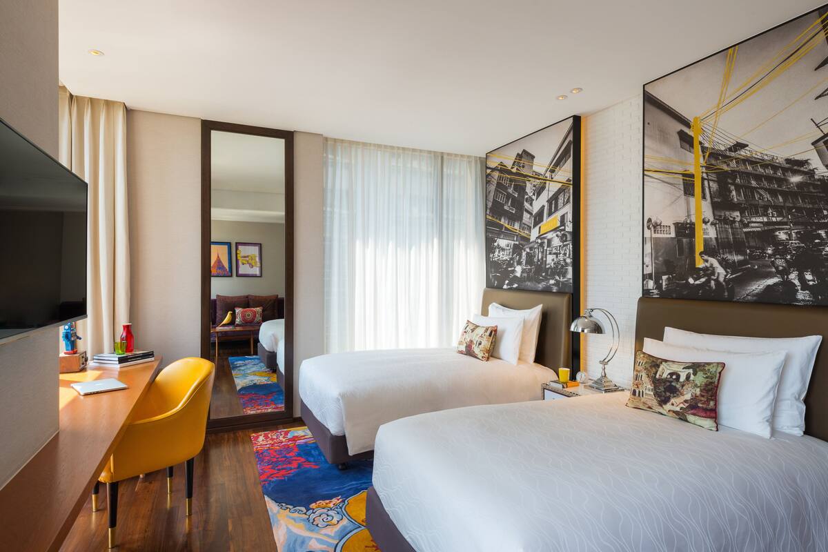 A hotel room with two beds, a desk, a chair, a TV, and a large mirror.