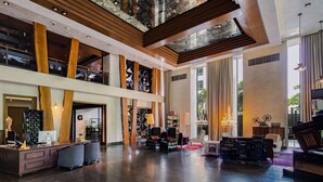 A spacious lobby with a high ceiling, wooden beams, a reception desk, seating area, and large windows allowing natural light.