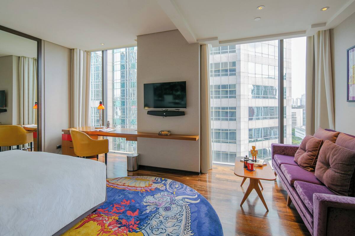 A hotel room with a bed, a desk, a sofa, a TV, and large windows with a city view.