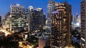 A high-rise hotel with a prominent 'HOTELS INDIGO' sign, surrounded by other modern buildings and busy streets at night.