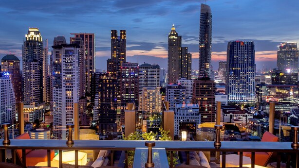 Vista panorámica de la ciudad desde una terraza en la azotea, con edificios modernos, una zona de comedor con sillas y mesas, y una barandilla.
