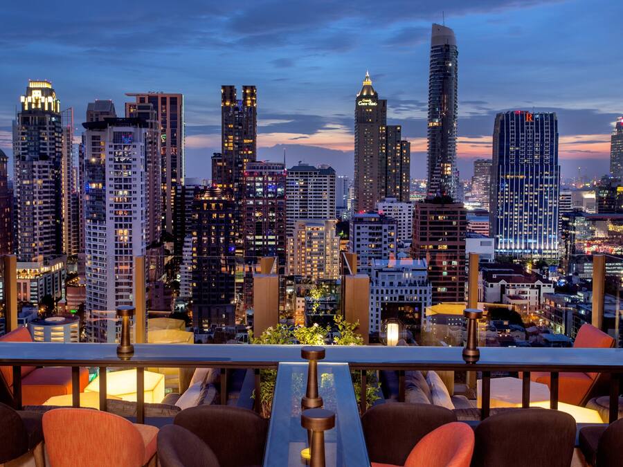 Vista panorámica de la ciudad desde una terraza en la azotea, con edificios modernos, una zona de comedor con sillas y mesas, y una barandilla.