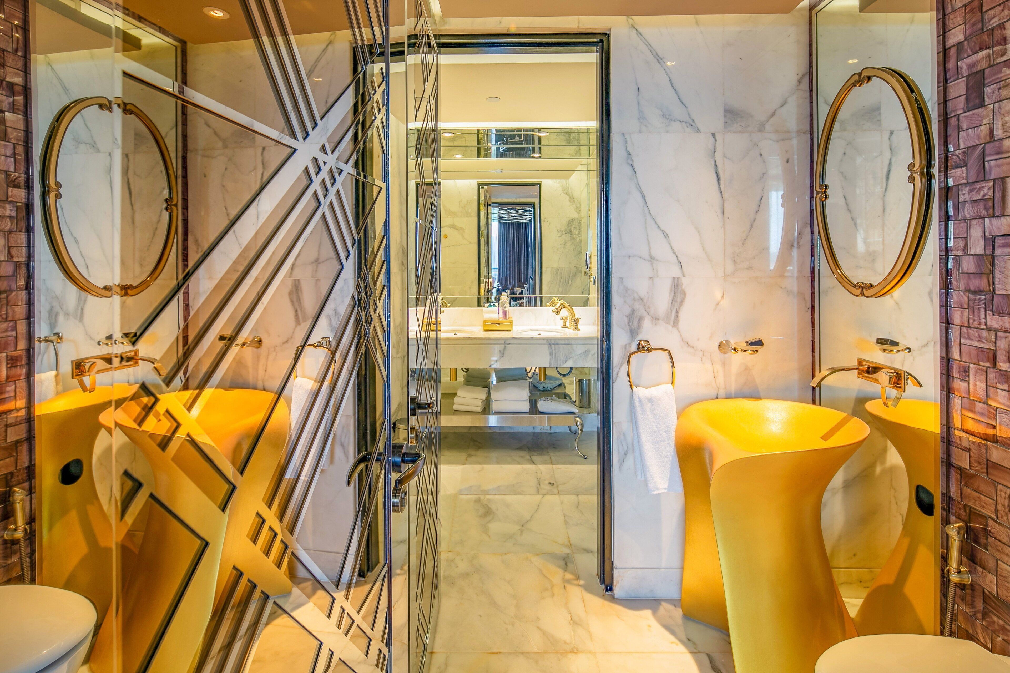 A modern bathroom with two large yellow sinks, a glass shower enclosure, and marble walls.