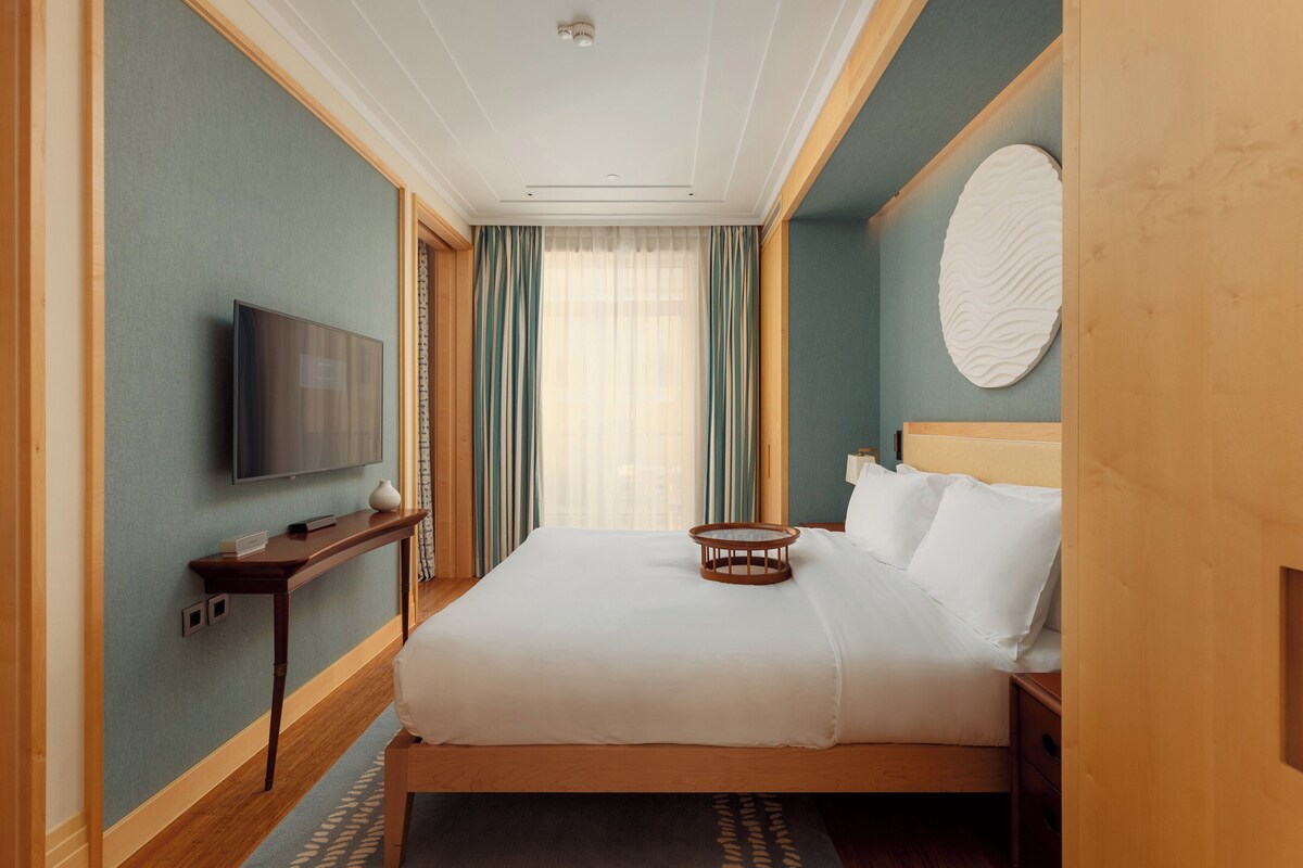 A hotel room with a bed, a television, a bedside table, and a wall-mounted decorative item.