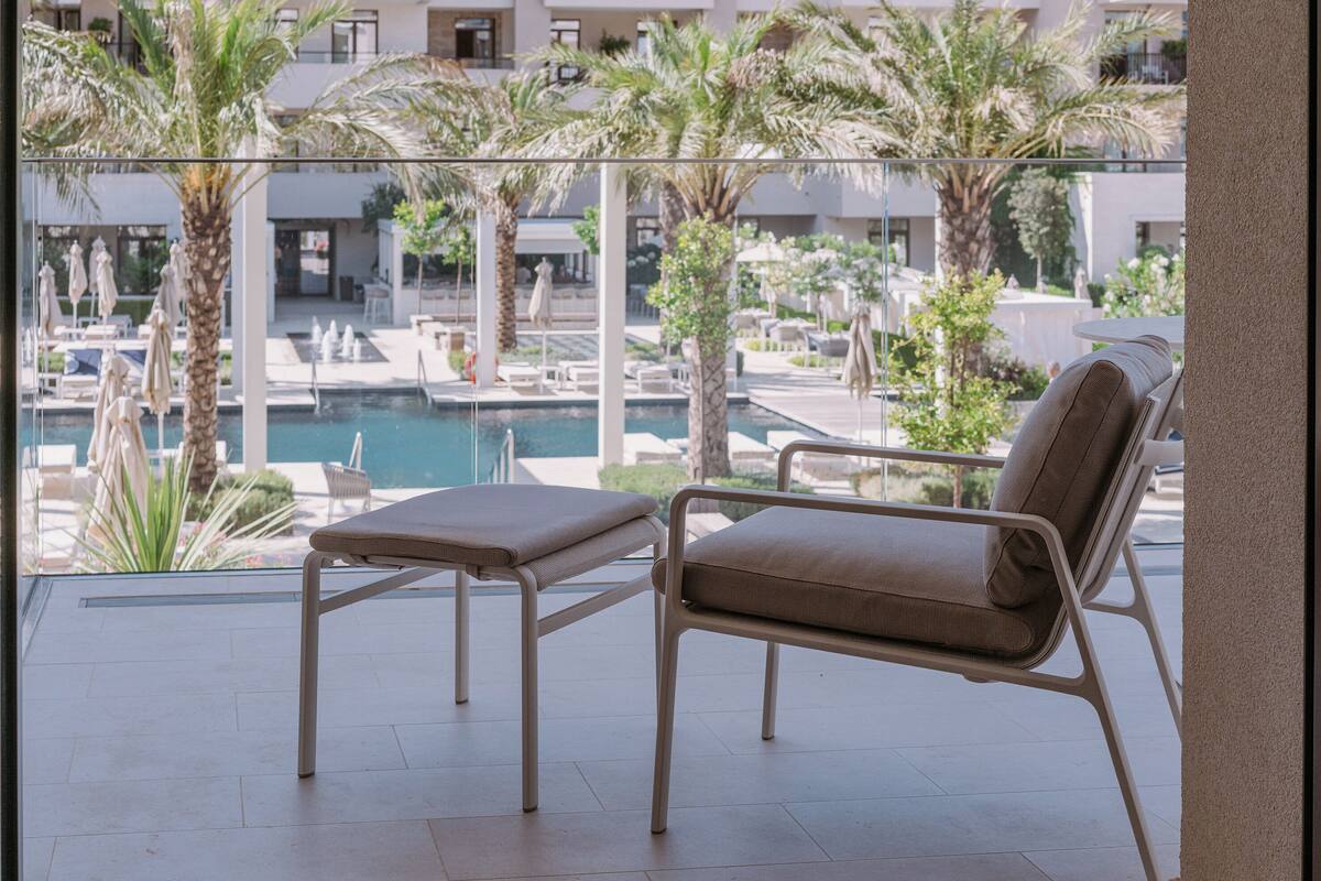 A balcony with a pool view, lounge chairs, and palm trees.
