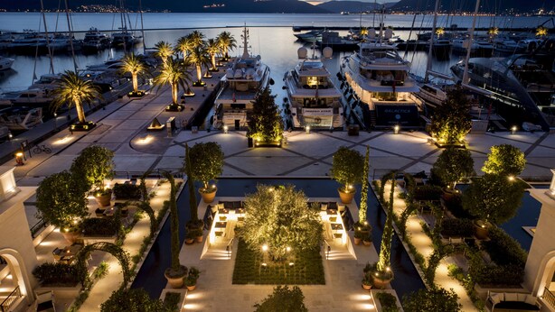 A marina with multiple yachts docked, surrounded by well-lit outdoor seating areas and palm trees. - Regent Porto Montenegro (Tivat)