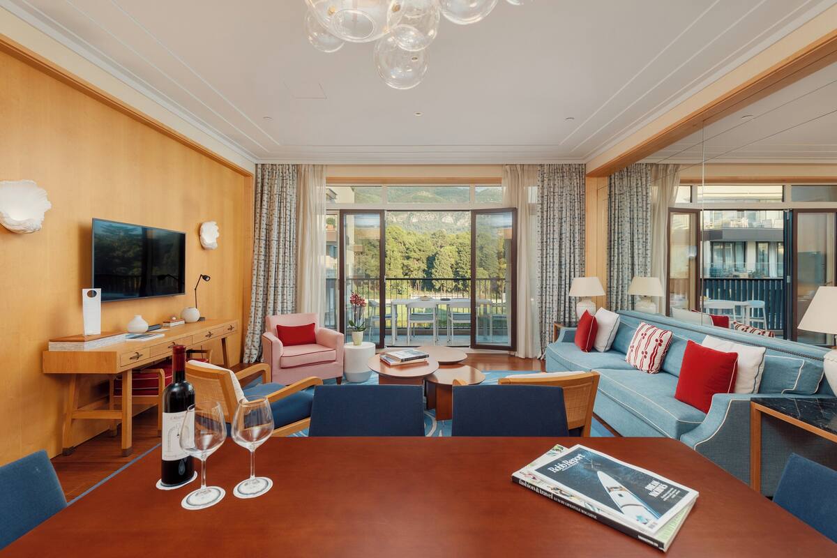 A hotel room with a dining area, a sofa, a TV, and a balcony with a view.