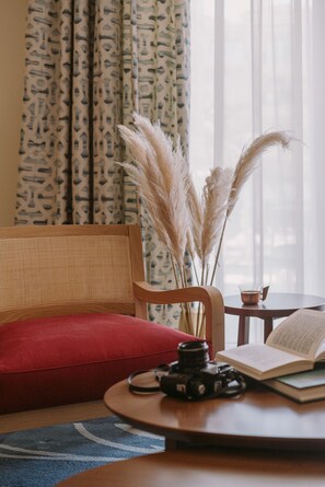 A cozy room with a wooden chair, a red cushion, a small round table with a camera, a book, and pampas grass. - Regent Porto Montenegro (Tivat)