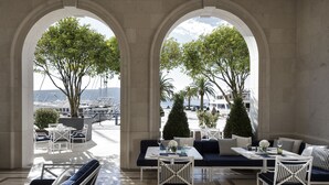 A covered outdoor seating area with tables and chairs, overlooking a marina with boats. - Regent Porto Montenegro (Tivat)
