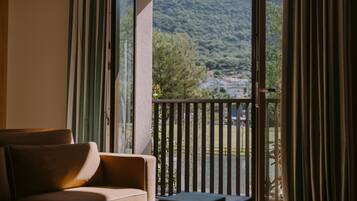 Una stanza con un divano e un tavolo, vista su un paesaggio verde attraverso un balcone con ringhiera.