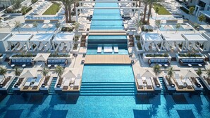A rooftop pool area with multiple lounge areas, palm trees, and a central water feature. - Regent Porto Montenegro (Tivat)