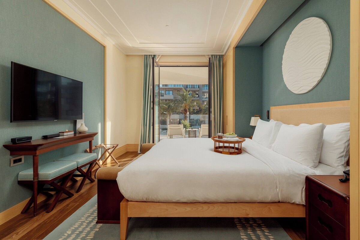 A hotel room with a large bed, a TV, a small table with a tray, and a view of the city through the window.