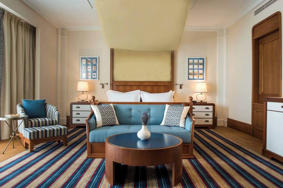 A hotel room with a large bed, two bedside tables with lamps, a sofa, a small side table, and a round coffee table.